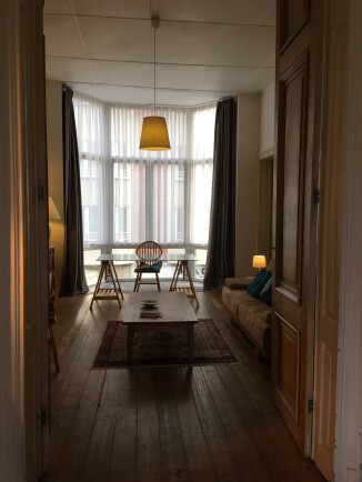 Ruime woonkamer hoge plafonds, logia met veel licht aan straatkant Originele houten deuren scheiden de slaapkamer.